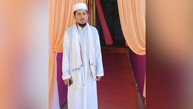 The image shows a man standing in white clothes in front of orange curtains