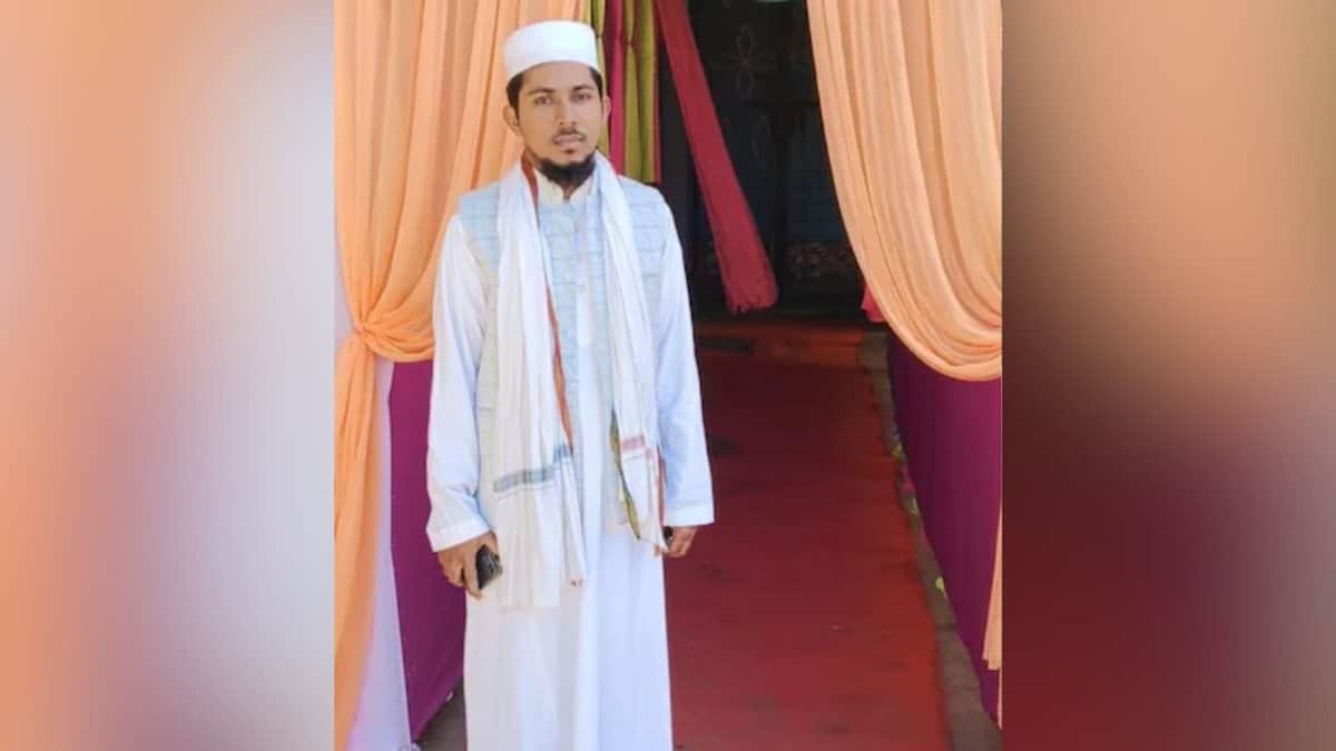 The image shows a man standing in white clothes in front of orange curtains