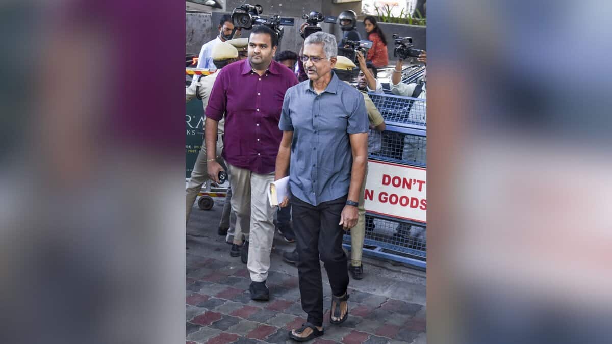 Two men walking on a street surrounded by media personnel with cameras, with police barricades visible in the background