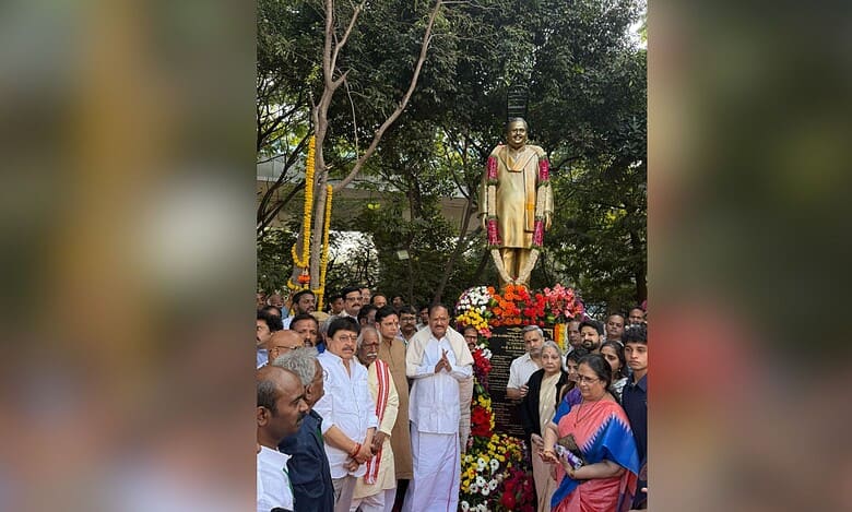 A gathering of dignitaries and attendees at the unveiling of S P Balasubrahmanyam's statue adorned with flower garlands at Ravindra Bharathi in Hyderabad, surrounded by lush trees.