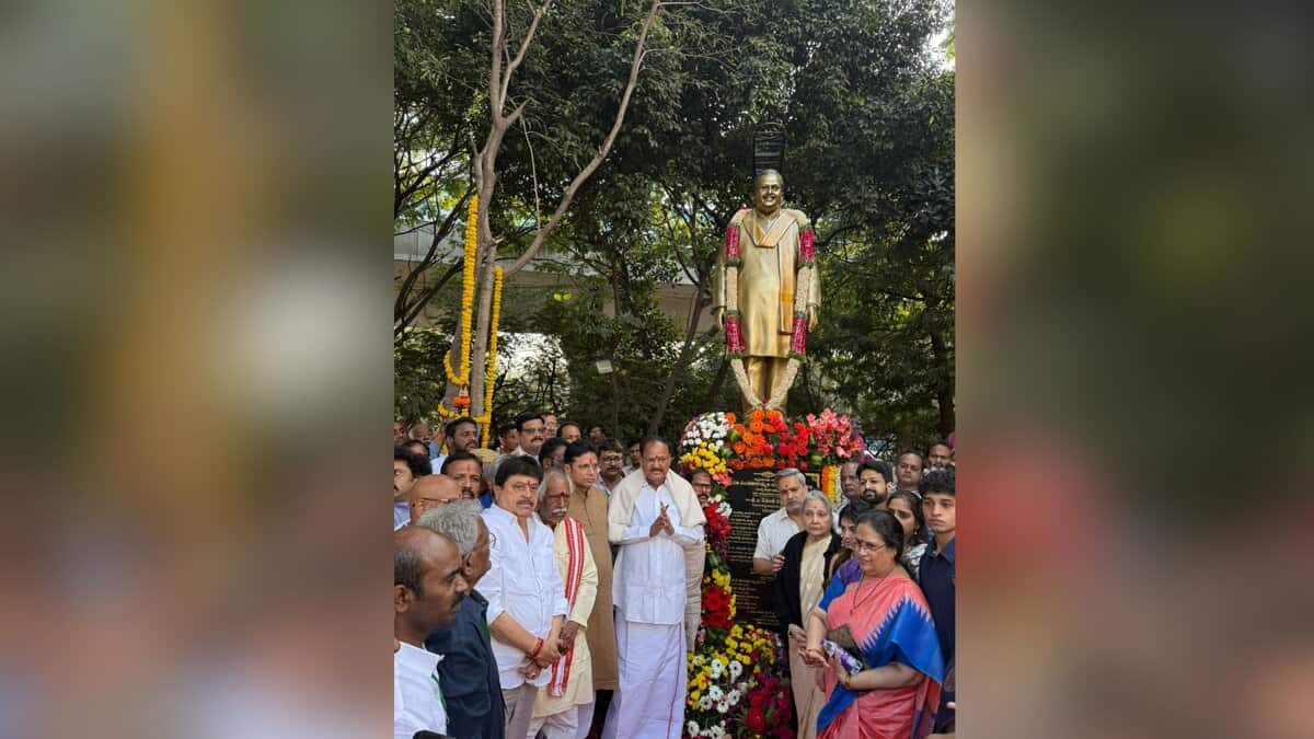 A gathering of dignitaries and attendees at the unveiling of S P Balasubrahmanyam's statue adorned with flower garlands at Ravindra Bharathi in Hyderabad, surrounded by lush trees.