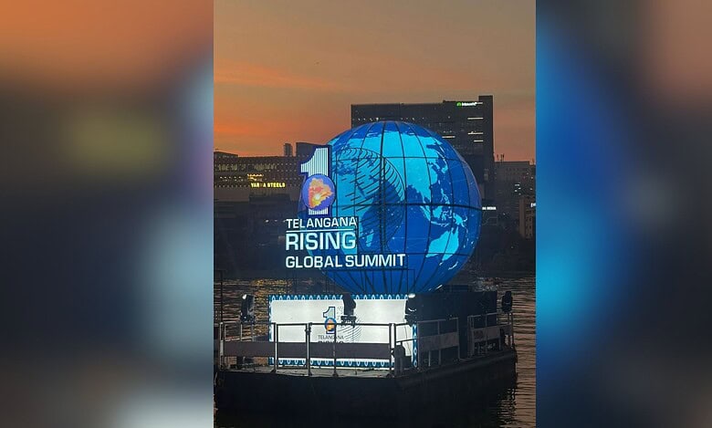 A large illuminated blue globe installation displays "Telangana Rising Global Summit" text against an urban skyline at dusk. The spherical structure features a world map design and is positioned on a waterfront platform with city buildings visible in the background.