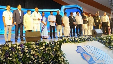 Large group of dignitaries standing on stage at a formal event with floral decorations and Telangana branding visible in the foreground.