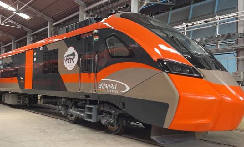 Image shows Modern orange and gray Vande Bharat Express train in maintenance facility