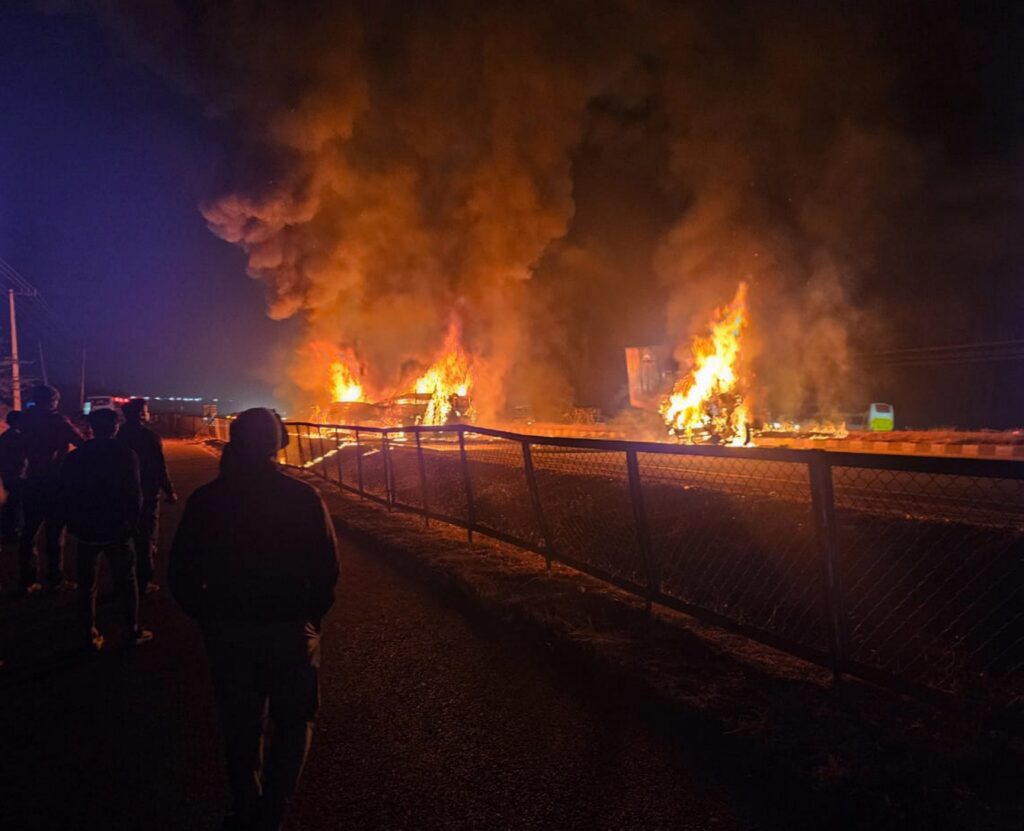 Accident on highway causes fire, drawing crowd of onlookers watching the blaze.