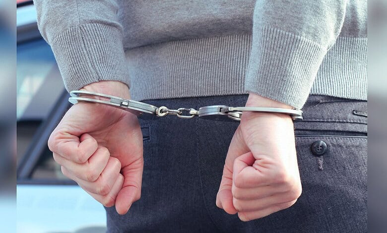 Image shows a person with their arms handcuffed behind their back
