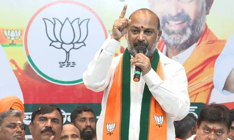 Bandi Sanjay in traditional white and saffron attire speaks passionately at a BJP event, gesturing with his finger raised while standing before the party's lotus symbol.