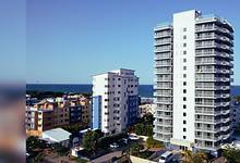 Modern white high-rise residential tower with curved balconies overlooking the ocean in a coastal urban setting