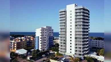 Modern white high-rise residential tower with curved balconies overlooking the ocean in a coastal urban setting