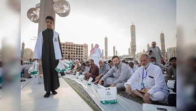 A young volunteer distributes Iftar meal boxes to worshippers seated at the Prophet’s Mosque in Madinah.