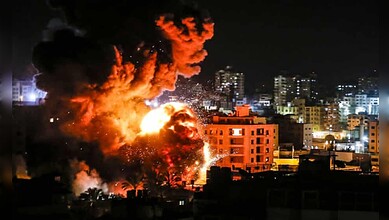 Explosion lights up buildings during Israeli air strike in Gaza City at night.