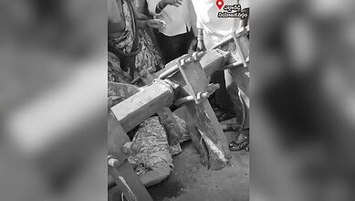 A black and white image showing a woman lying under a tractor.