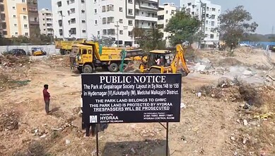 Image shows Public notice sign by HYDRAA at cleared construction site with apartments and heavy machinery in background