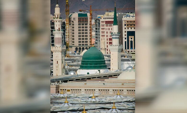 The green dome and minarets of the Prophet’s Mosque in Madinah, with surrounding buildings visible in the background.