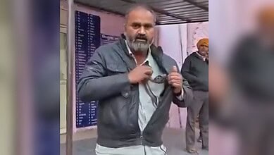 Image shows a man wearing a gray jacket and holding a snake stands in what appears to be a public space