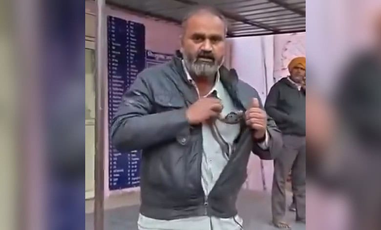 Image shows a man wearing a gray jacket and holding a snake stands in what appears to be a public space