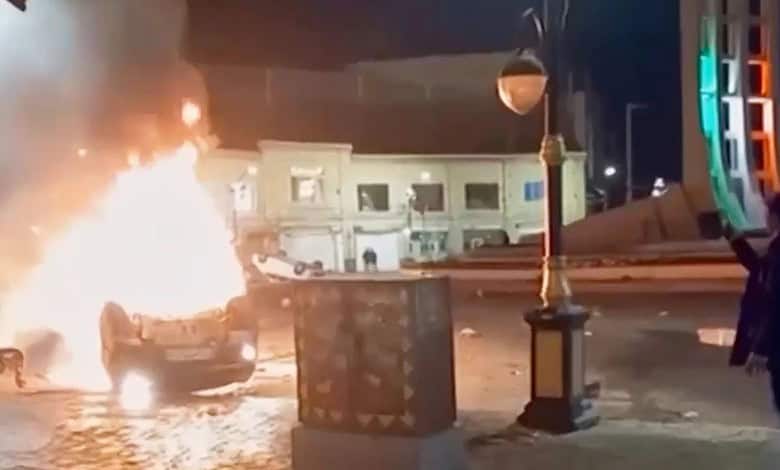 This frame grab from a video released Friday, January 9, by Iranian state television shows a man holding a device to document burning vehicles during a night of mass protests in Zanjan, Iran.