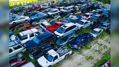 Image shows Aerial view of a densely packed salvage yard filled with various damaged and end-of-life vehicles in multiple colors.
