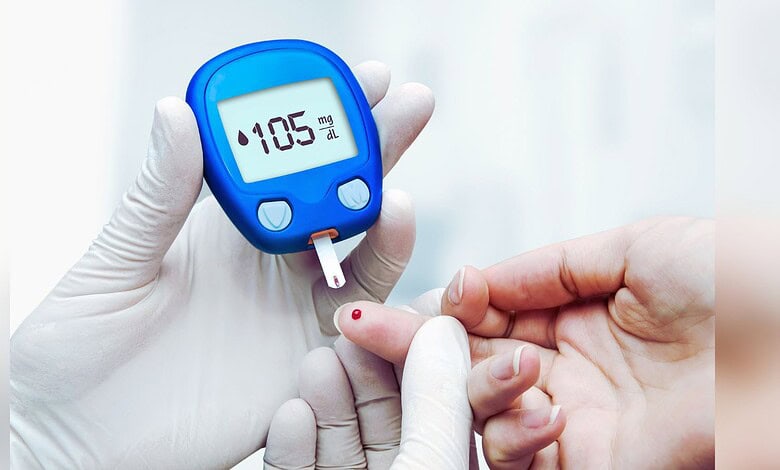 Image shows A healthcare worker in gloves performing a blood glucose test on a patient's finger with a blue glucometer