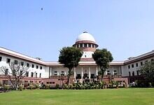 View of the Supreme Court of India with lush green lawn and trees in front.