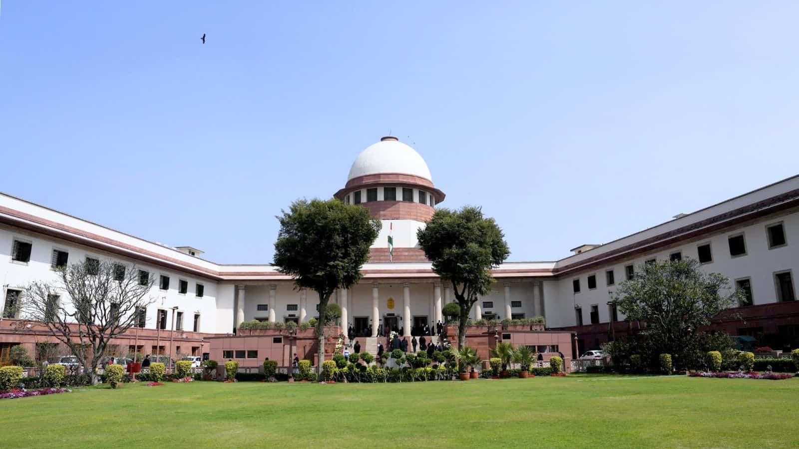 View of the Supreme Court of India with lush green lawn and trees in front.