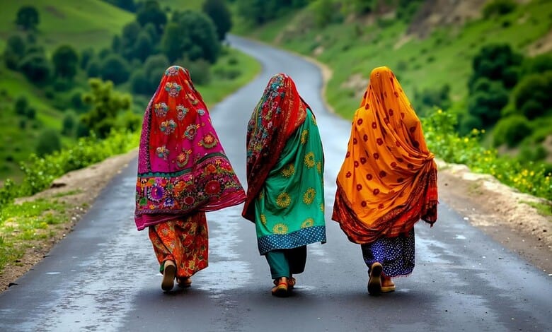 Women walking on a rural road in colourful traditional attire, green hills in the background.