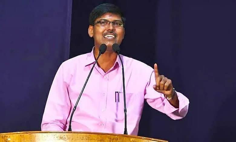 Man speaking at a conference, wearing pink shirt, gesturing with his finger, standing behind a podium wit.