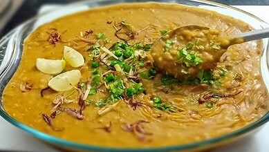 Traditional Hyderabadi Haleem served in a glass dish with garnishes, highlighting regional culinary diver.