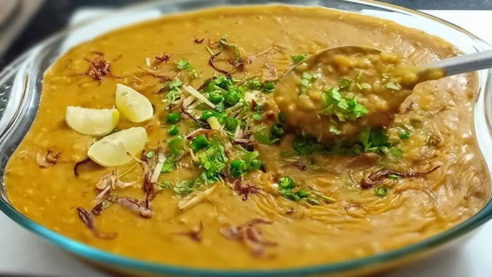 Traditional Hyderabadi Haleem served in a glass dish with garnishes, highlighting regional culinary diver.