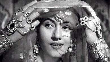 Woman in traditional Indian bridal attire with jewelry and veil, smiling softly.