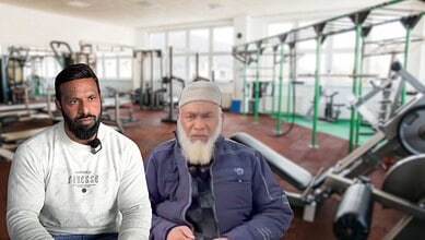 Two men in casual attire talking inside a well-equipped gym.