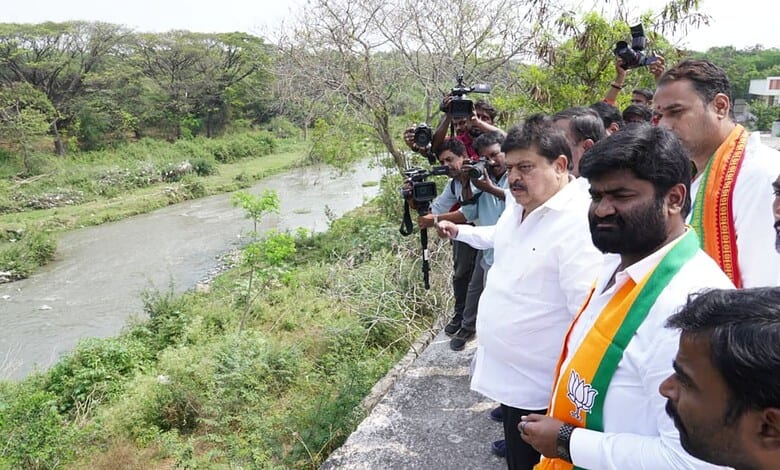 Politicians and media at riverbank during environmental cleanup activity.