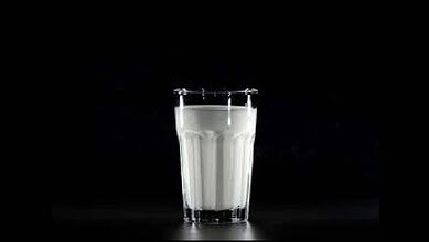 Glass of milk with a metal clamp on a dark background.