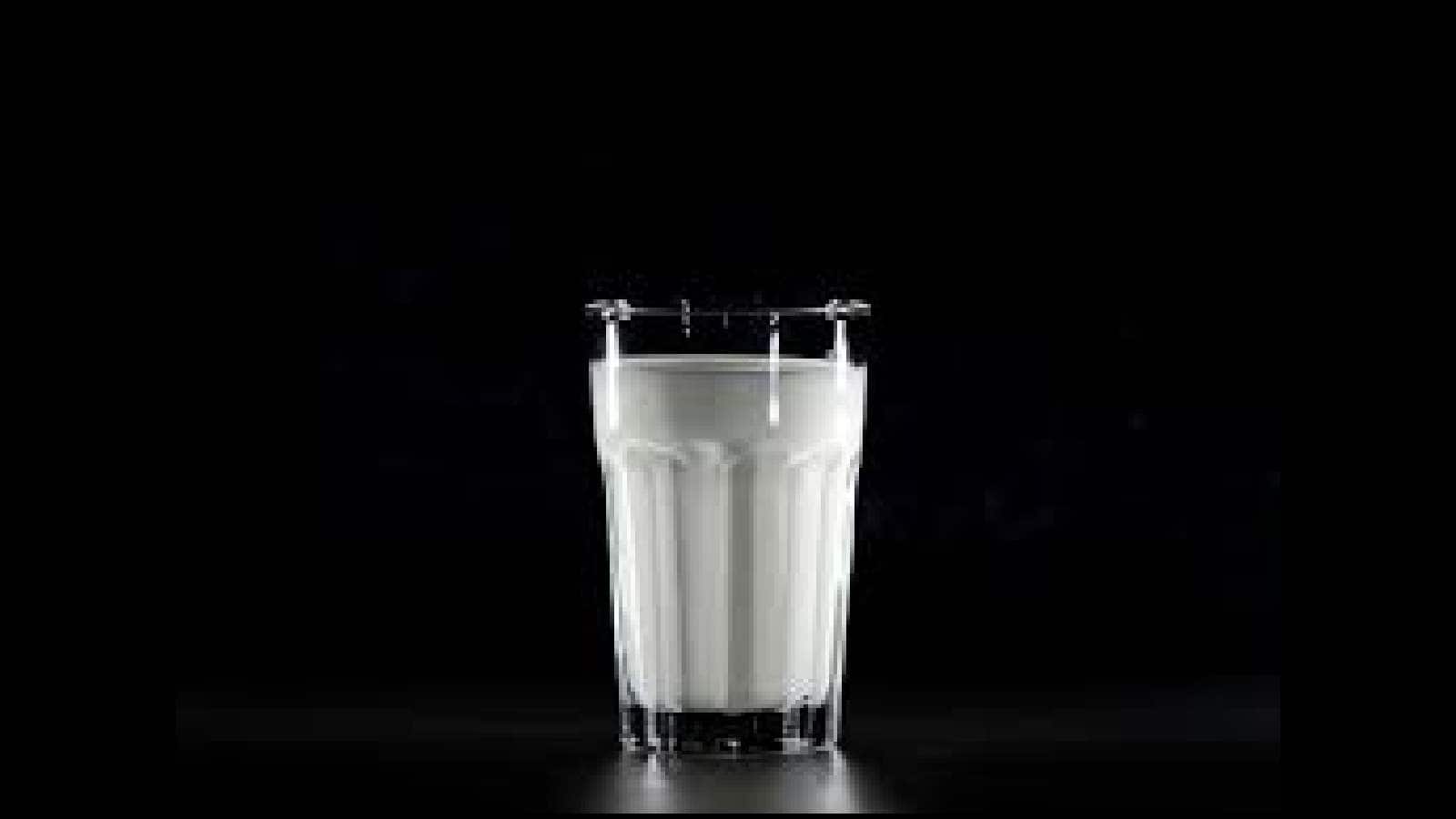 Glass of milk with a metal clamp on a dark background.