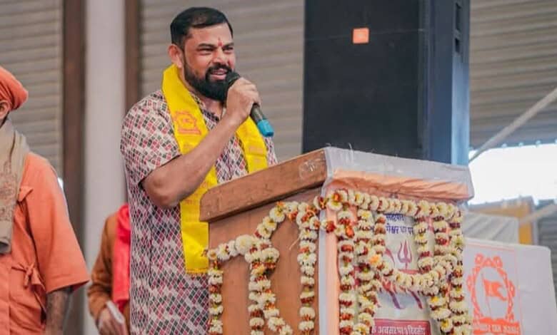 Raja Singh speaking at a rally with a microphone, wearing a yellow scarf, during a political gatheri.