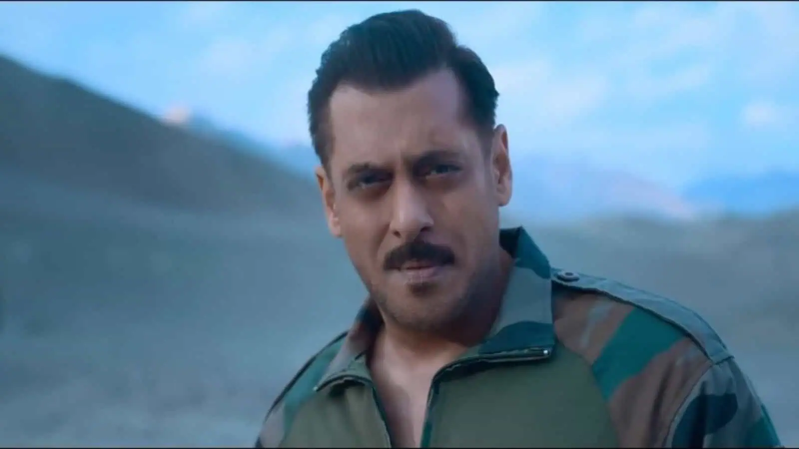 A man in military attire outdoors with mountains in the background.