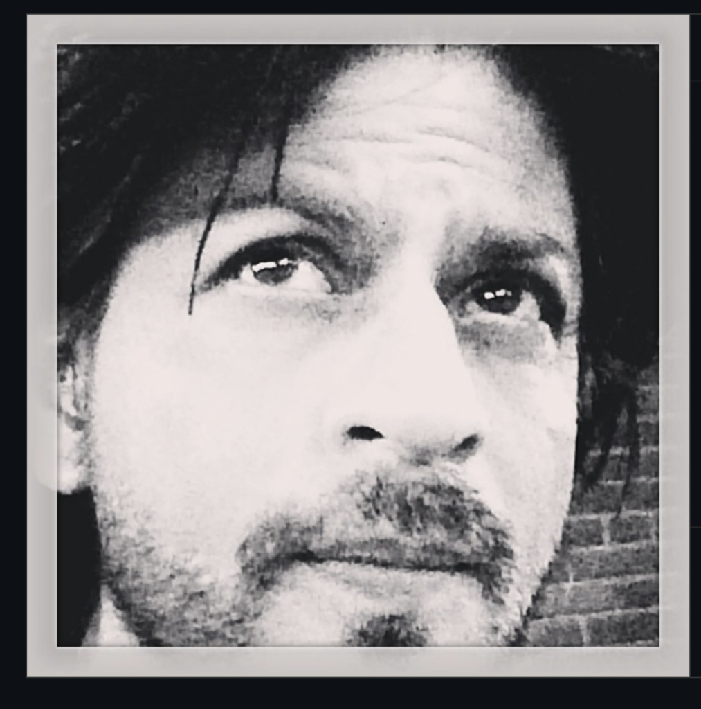 Close-up of a man with beard and long hair in black and white.