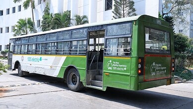 Electric bus parked on city street with modern buildings in background.