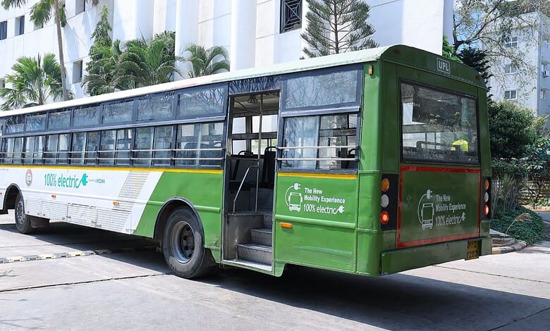 Electric bus parked on city street with modern buildings in background.