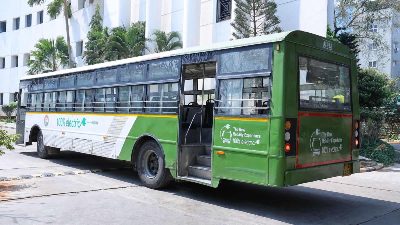 Electric bus parked on city street with modern buildings in background.