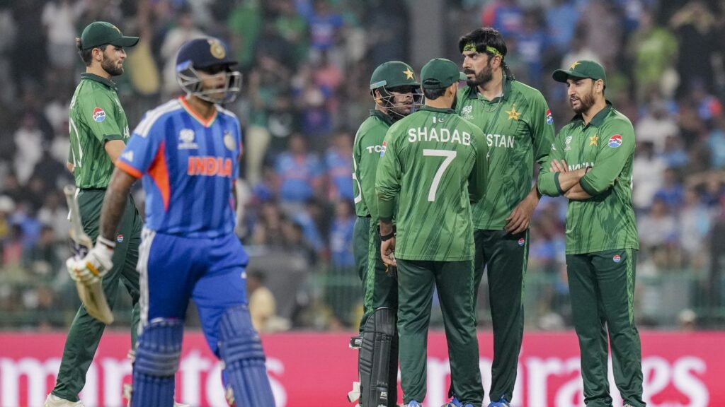 Pakistan players in green uniforms on the cricket field with Indian players in blue.