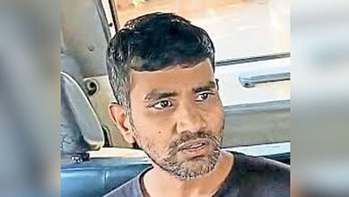 Man with short black hair and beard sitting in a vehicle, looking serious.