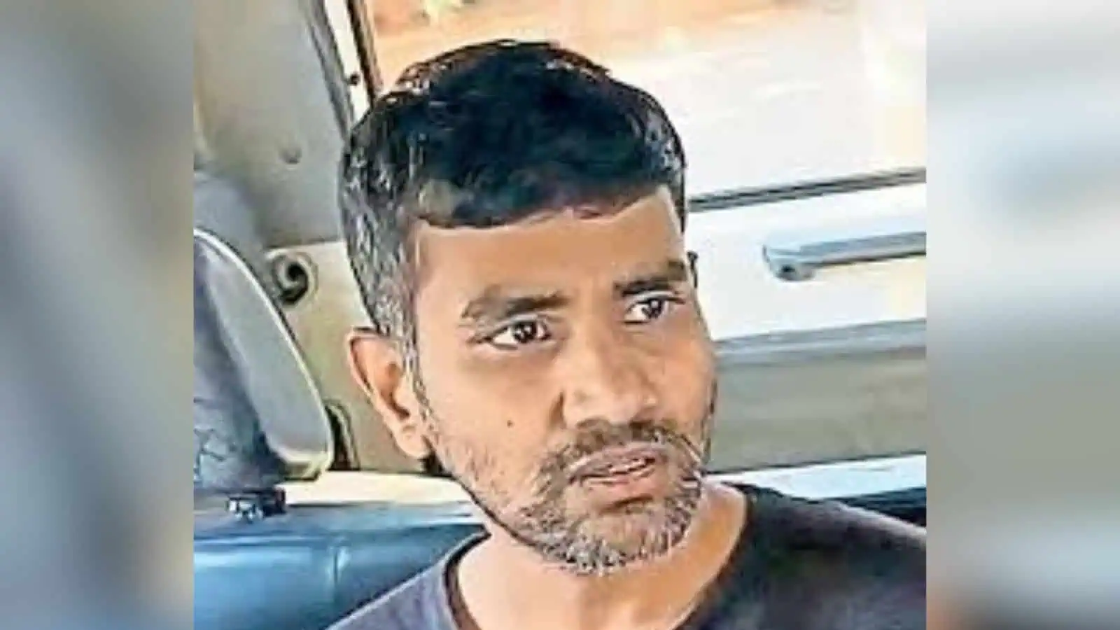 Man with short black hair and beard sitting in a vehicle, looking serious.