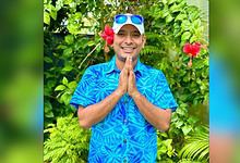 Anvesh smiling outdoors wearing sunglasses, surrounded by tropical plants and flowers.