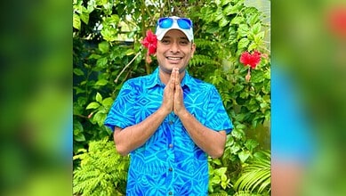 Anvesh smiling outdoors wearing sunglasses, surrounded by tropical plants and flowers.