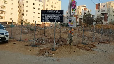 Fenced construction area in Hyderabad with urban buildings and a public notice sign.