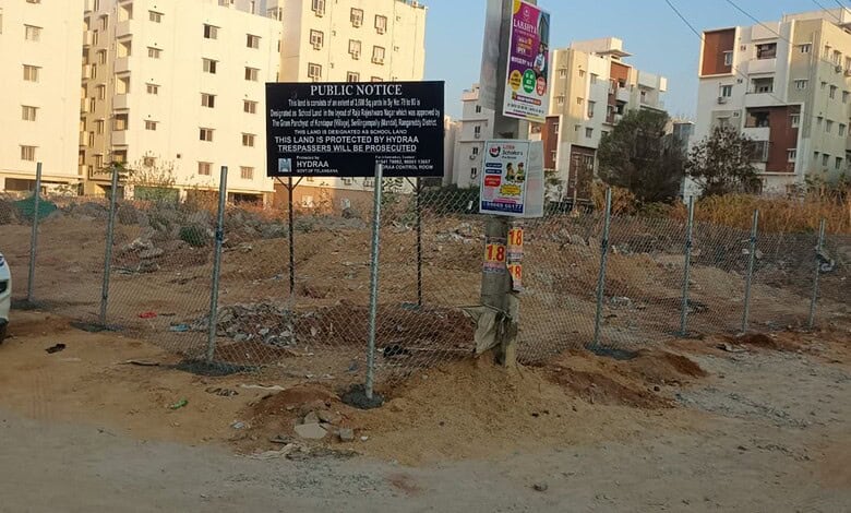 Fenced construction area in Hyderabad with urban buildings and a public notice sign.