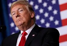 Donald Trump speaking at a press event with US flags behind him.