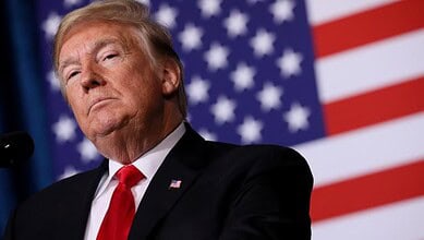 Donald Trump speaking at a press event with US flags behind him.