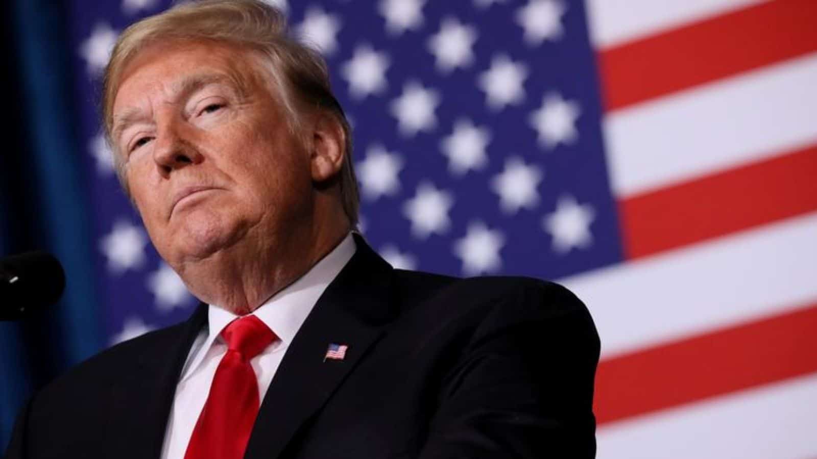 Donald Trump speaking at a press event with US flags behind him.